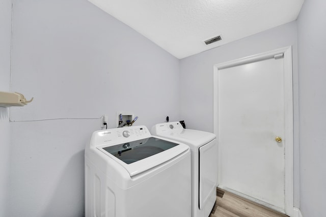 washroom featuring light wood-type flooring, washing machine and dryer, and a textured ceiling