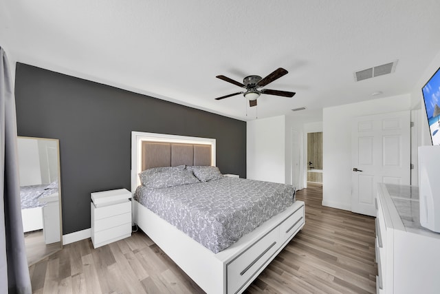 bedroom with ceiling fan, a textured ceiling, light hardwood / wood-style flooring, and connected bathroom