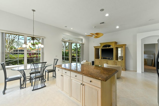 kitchen featuring ceiling fan, a center island, dark stone counters, decorative light fixtures, and light tile patterned flooring