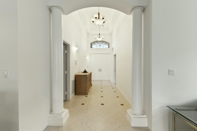 corridor with light tile patterned floors, a towering ceiling, decorative columns, and an inviting chandelier