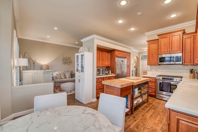 kitchen featuring ornamental molding, butcher block counters, a center island, dark wood-type flooring, and stainless steel appliances