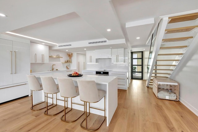 kitchen with white cabinets, a center island, sink, a breakfast bar, and light hardwood / wood-style flooring