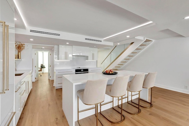 kitchen with a kitchen bar, black oven, white cabinetry, and a center island