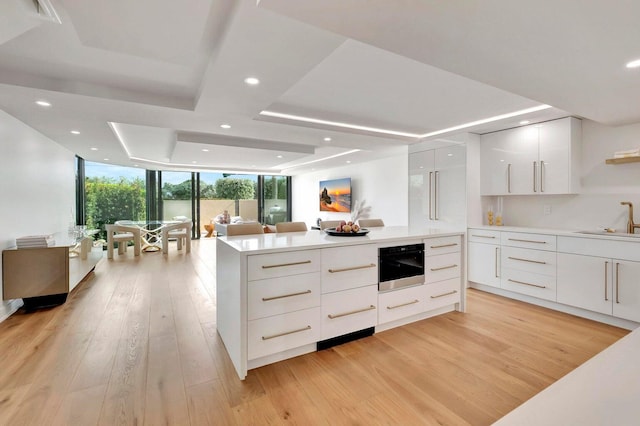 kitchen featuring light hardwood / wood-style floors, a raised ceiling, white cabinets, expansive windows, and sink