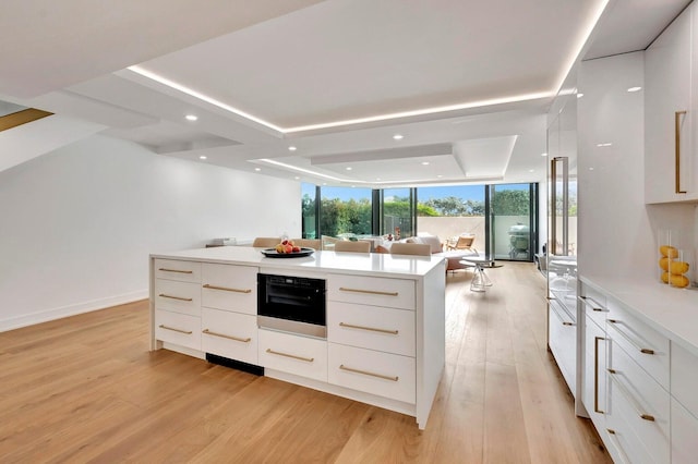 kitchen featuring white cabinetry, a wall of windows, a raised ceiling, and light hardwood / wood-style flooring