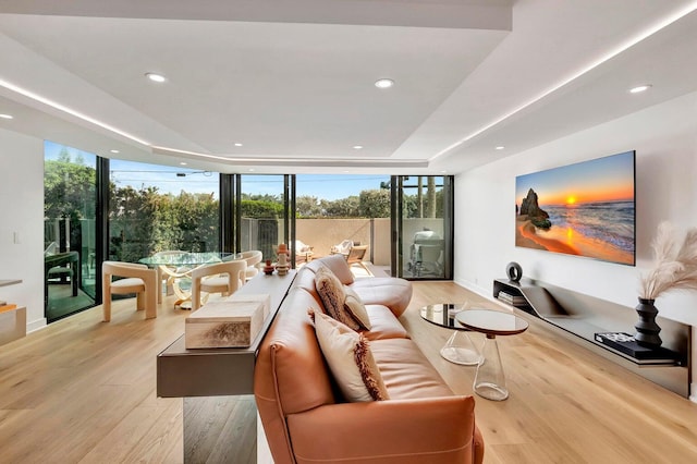 living room with a raised ceiling, plenty of natural light, floor to ceiling windows, and light hardwood / wood-style flooring