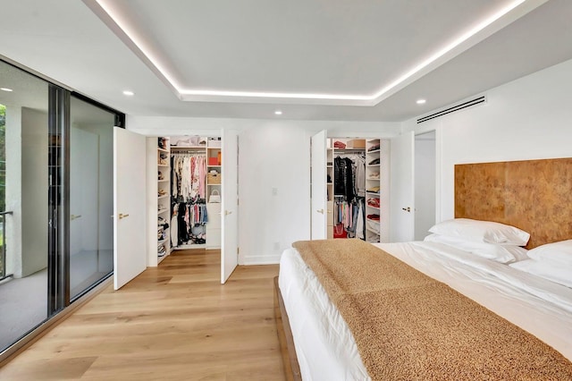 bedroom with a spacious closet, a tray ceiling, and light hardwood / wood-style floors