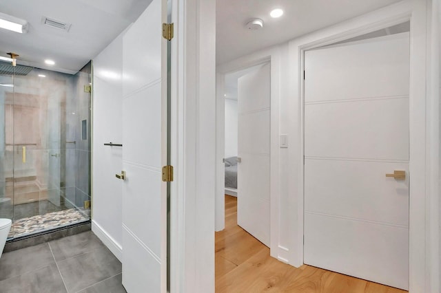 bathroom featuring a shower with shower door, wood-type flooring, and toilet