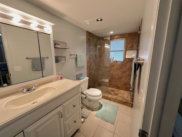 bathroom featuring vanity, toilet, a tile shower, and tile patterned flooring