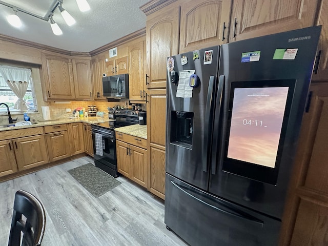 kitchen featuring light stone counters, a textured ceiling, light wood-type flooring, sink, and stainless steel appliances