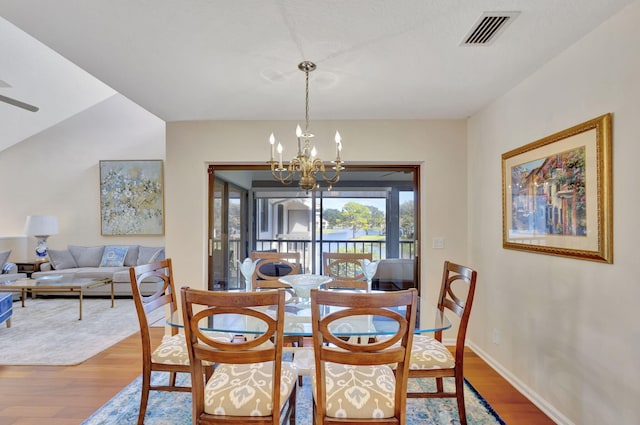 dining area with hardwood / wood-style floors, ceiling fan with notable chandelier, and vaulted ceiling