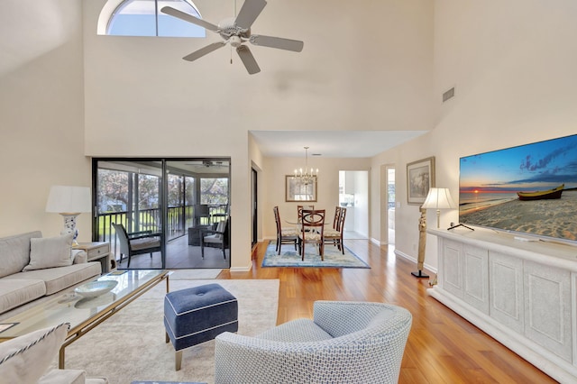 living room featuring plenty of natural light, a towering ceiling, ceiling fan with notable chandelier, and light wood-type flooring