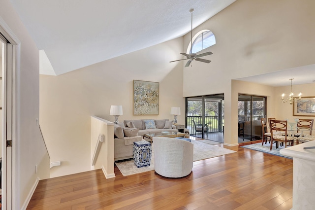 living room featuring high vaulted ceiling, ceiling fan with notable chandelier, and hardwood / wood-style flooring