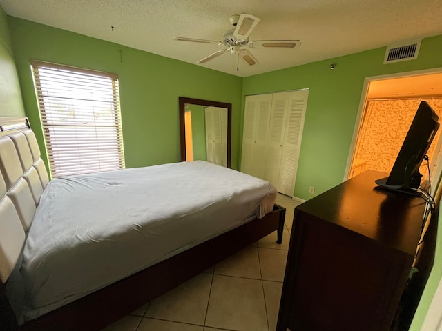 bedroom with ceiling fan, a textured ceiling, light tile patterned floors, and a closet