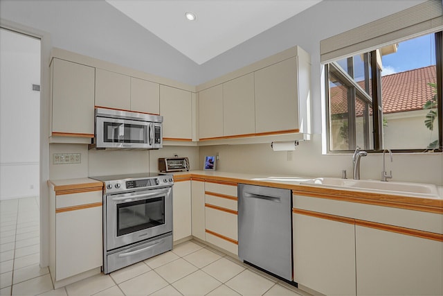 kitchen featuring lofted ceiling, sink, light tile patterned flooring, and stainless steel appliances