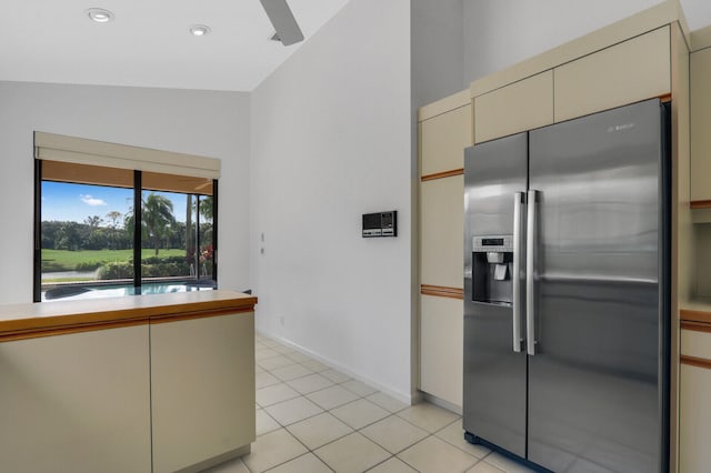 kitchen with light tile patterned flooring, stainless steel fridge with ice dispenser, vaulted ceiling, and cream cabinetry