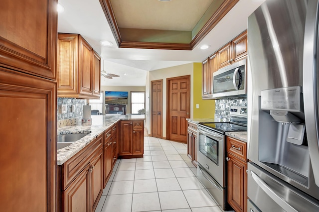 kitchen featuring sink, a raised ceiling, light stone counters, and appliances with stainless steel finishes