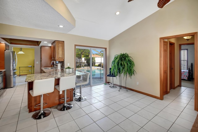 kitchen with sink, stainless steel fridge, light stone countertops, kitchen peninsula, and a breakfast bar area