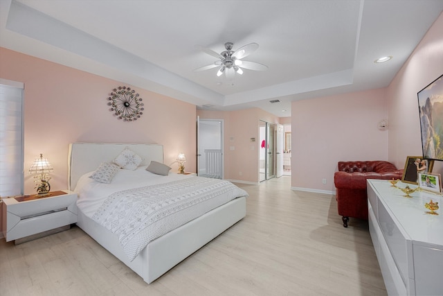 bedroom with ceiling fan, a tray ceiling, and light hardwood / wood-style flooring