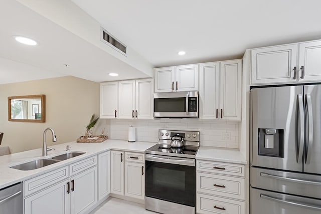 kitchen featuring stainless steel appliances, white cabinets, kitchen peninsula, sink, and tasteful backsplash