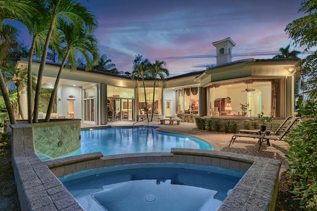 pool at dusk featuring ceiling fan, a patio area, and an in ground hot tub