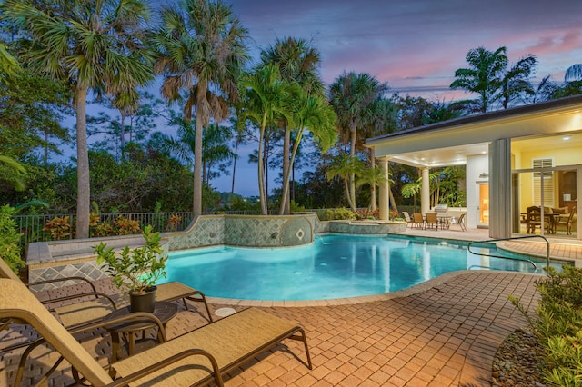 pool at dusk with a hot tub and a patio area