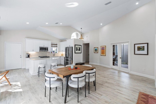 dining room with light hardwood / wood-style floors, high vaulted ceiling, and french doors