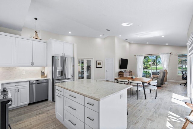 kitchen featuring appliances with stainless steel finishes, light wood-type flooring, decorative light fixtures, a center island, and white cabinetry