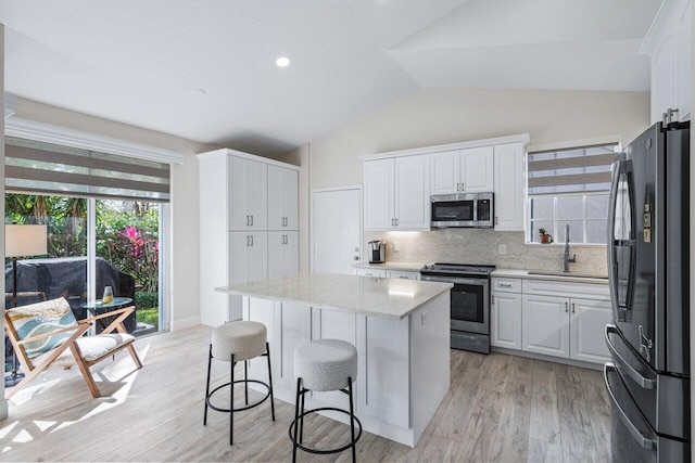 kitchen featuring white cabinetry, sink, a center island, vaulted ceiling, and appliances with stainless steel finishes