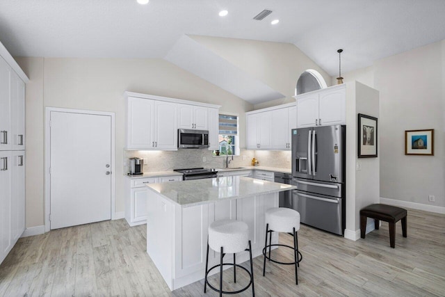 kitchen with a center island, white cabinets, lofted ceiling, and appliances with stainless steel finishes