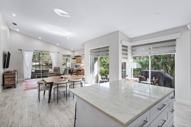 kitchen with light wood-type flooring, light stone counters, vaulted ceiling, a center island, and white cabinetry