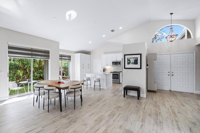 dining room with light hardwood / wood-style floors, high vaulted ceiling, and a notable chandelier