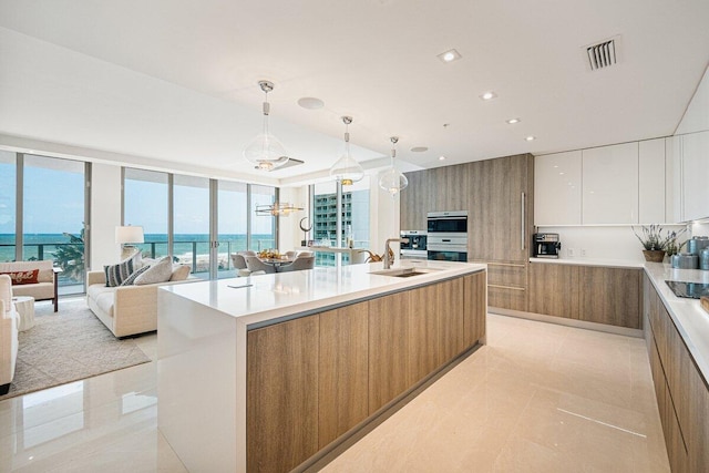 kitchen with decorative light fixtures, sink, white cabinets, a water view, and a kitchen island with sink