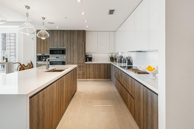 kitchen with sink, a large island with sink, decorative light fixtures, double oven, and white cabinets