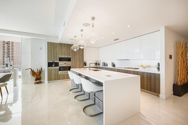 kitchen with hanging light fixtures, a breakfast bar, white cabinets, double oven, and a kitchen island with sink