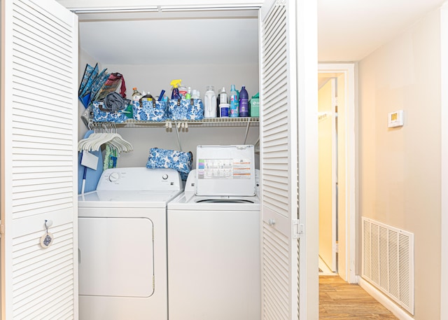 clothes washing area with washer and clothes dryer and light wood-type flooring