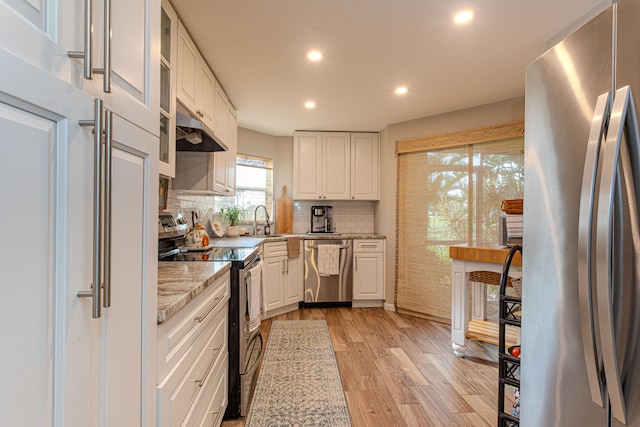 kitchen with stainless steel appliances, light stone counters, backsplash, white cabinets, and light wood-type flooring