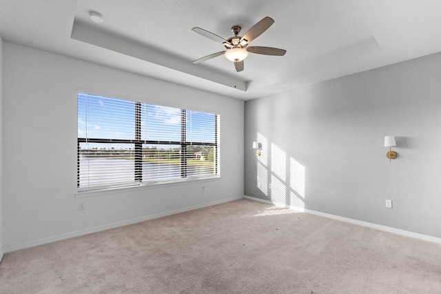 carpeted empty room with ceiling fan and a raised ceiling