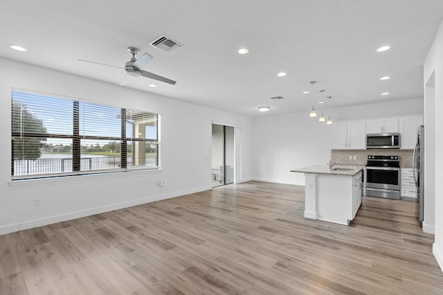 kitchen with white cabinets, an island with sink, appliances with stainless steel finishes, pendant lighting, and light hardwood / wood-style floors