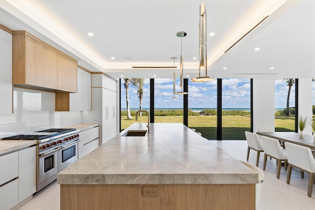 kitchen featuring pendant lighting, sink, white cabinetry, double oven range, and a center island with sink