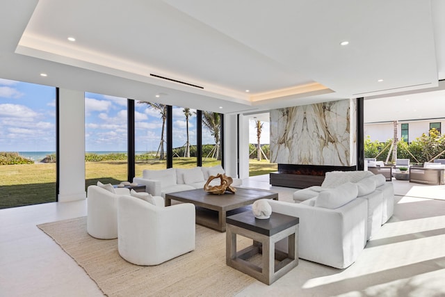 living room featuring a raised ceiling, expansive windows, and a water view