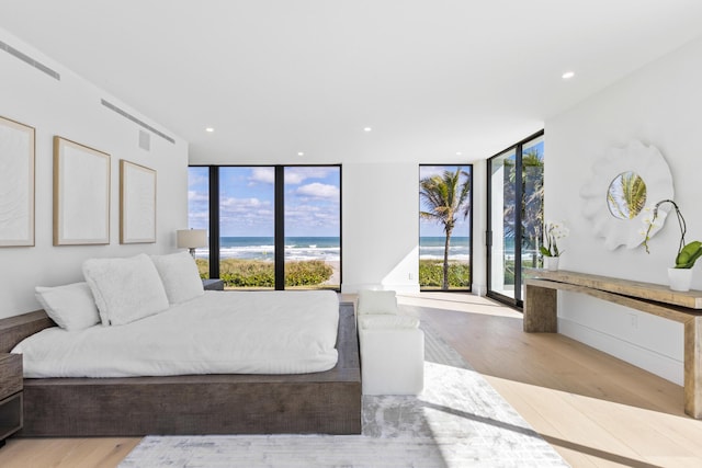 bedroom featuring a view of the beach, light wood-type flooring, floor to ceiling windows, and a water view