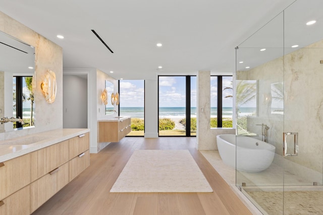 bathroom with shower with separate bathtub, wood-type flooring, vanity, floor to ceiling windows, and a water view