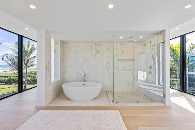 bathroom featuring tile walls, hardwood / wood-style flooring, a wall of windows, and plus walk in shower