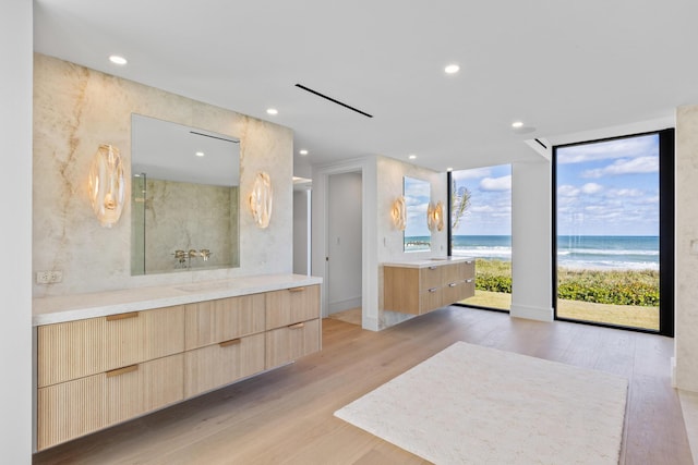 bathroom with hardwood / wood-style floors, a view of the beach, expansive windows, vanity, and a water view