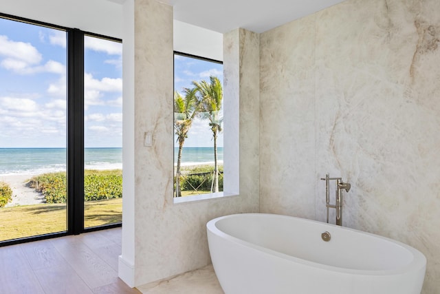 bathroom with a water view, a view of the beach, hardwood / wood-style floors, and a tub