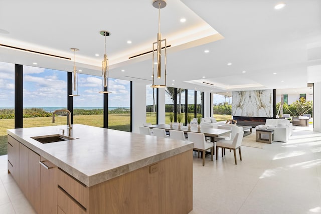 kitchen featuring pendant lighting, sink, a spacious island, a tray ceiling, and expansive windows