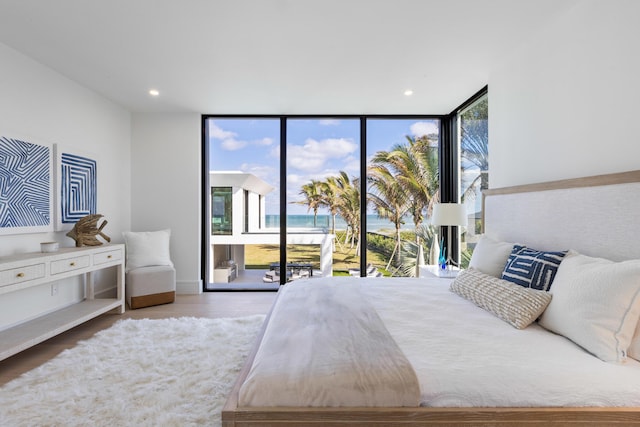 bedroom with access to outside, light hardwood / wood-style floors, floor to ceiling windows, and a water view