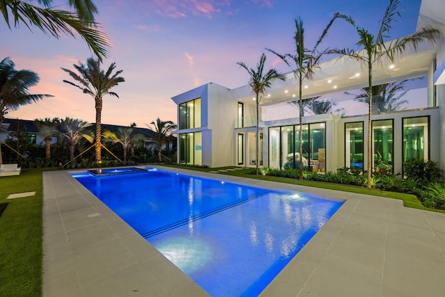 pool at dusk featuring an in ground hot tub and a patio