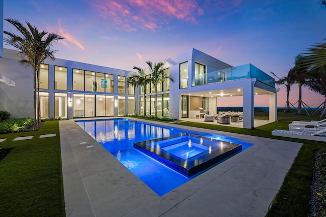 pool at dusk with an in ground hot tub, an outdoor hangout area, and a patio area